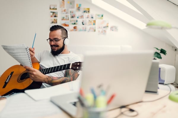 Musician writes on sheet music with acoustic guitar in hand